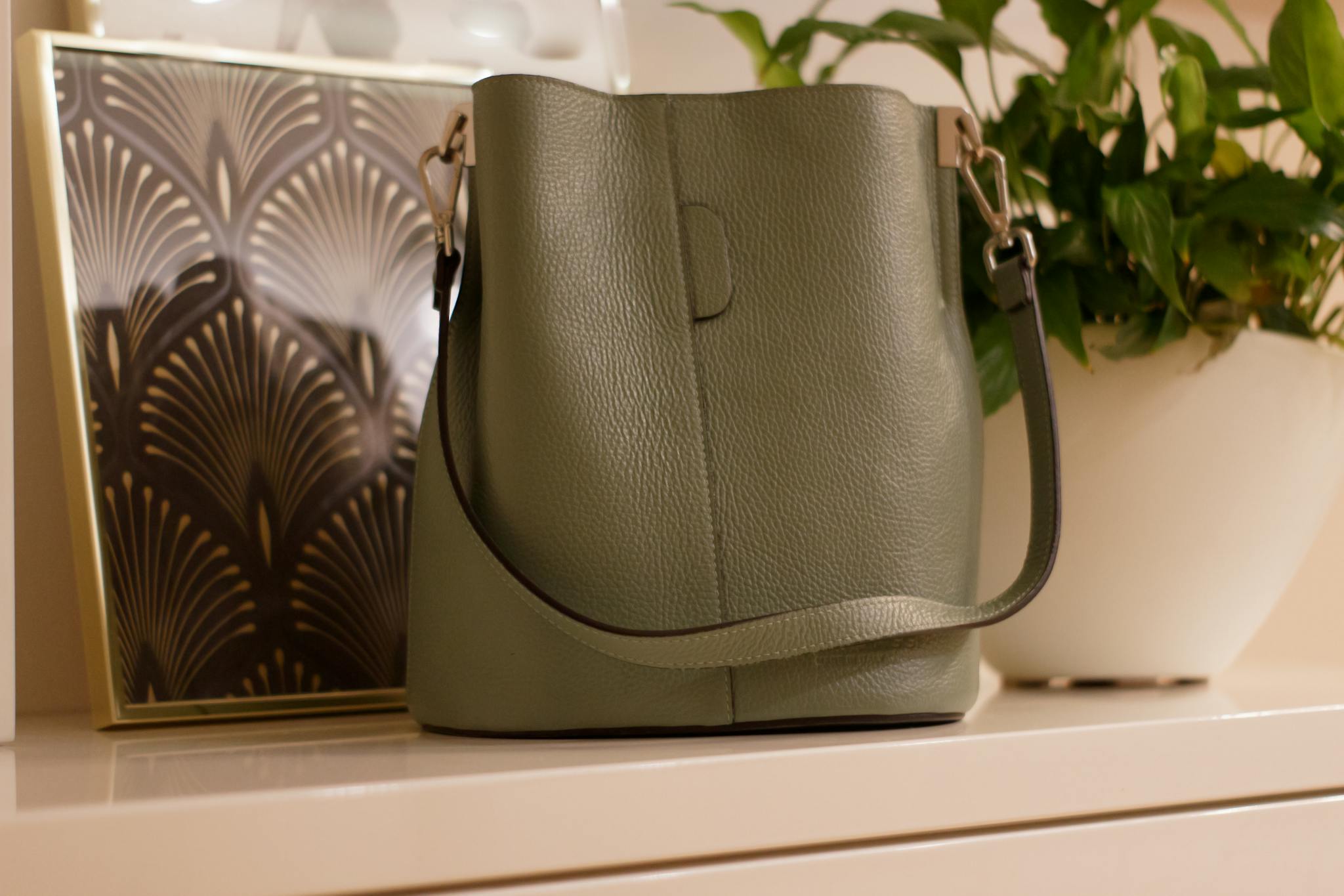 Elegant green leather bag on modern dresser with houseplant.